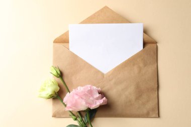 Boş kart, zarf ve çiçekler bej arka planda, düz konum