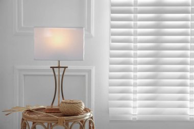 Şık bir lamba, kuru yaprak ve kapalı alandaki beyaz duvarın yanındaki rattan masasında hasır bir kutu. Metin için boşluk