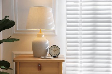 Beyaz duvarın yanındaki komodinin üzerinde şık bir lamba, yüzükler ve çalar saat. Metin için boşluk