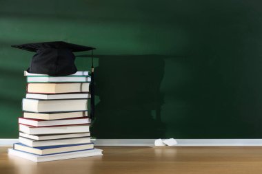 Öğretmenler Günün kutlu olsun. Kara tahtanın yanındaki ahşap masada kitap ve havan topu yığını, metin için boşluk