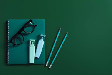 Öğretmenler günün kutlu olsun. Not defteri, kırtasiye malzemesi ve yeşil arka planda gözlük. Metin için boşluk