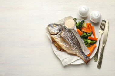 Tuz, karabiber, kızarmış dorado balığı, sebze, sos ve çatal bıçak takımı açık ahşap masa, düz yatak. Metin için boşluk