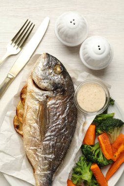 Tuz, karabiber, kızarmış dorado balığı, sebze, sos ve çatal bıçak takımı açık ahşap masada, düz yerde.