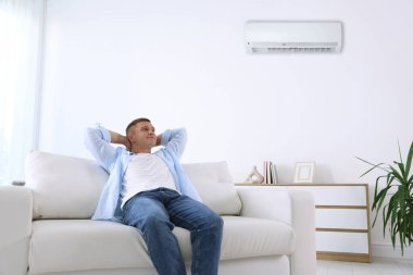 Evdeki kanepedeki klima sayesinde adam rahat sıcaklığın tadını çıkarıyor.