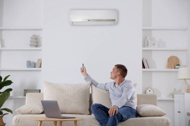 Evdeki kanepede uzaktan kumandalı bir adam klimayı açıyor.