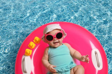Güneş gözlüklü şirin bir bebek ve yüzme havuzunda pembe şişirilebilir bir yüzük. Üst görünüm