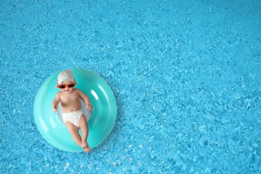 Güneş gözlüklü, yüzme havuzunda şişme yüzük takan şirin bir bebek. Üst görünüm