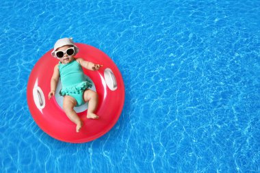 Güneş gözlüklü şirin bir bebek ve yüzme havuzunda pembe şişirilebilir bir yüzük. Üst görünüm