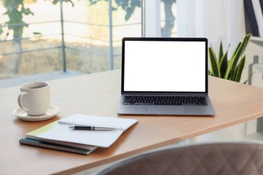 Boş beyaz ekranlı ve masadaki kırtasiyeli dizüstü bilgisayar. Rahat ev işyeri