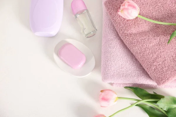 Bir yığın temiz havlu, kozmetik ürünler ve beyaz masa üzerinde lale çiçekleri.