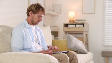 Evdeki koltukta dizüstü bilgisayar kullanan bir adam.