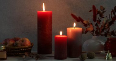 Masanın üzerinde gri arka planda farklı yanan mumlar olan kompozisyon. Sonbahar atmosferi