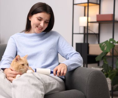 Tiftik silindirli gülümseyen kadın evdeki kanepede kedisinin saçlarını temizliyor.