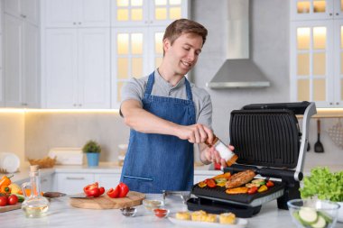 Adam sebzelere tuz ve mutfakta ızgarada et pişiriyor.