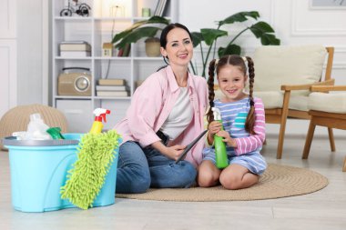 Küçük yardımcı. Evde farklı temizlik ürünleri ve malzemeleriyle anne ve kızı var.