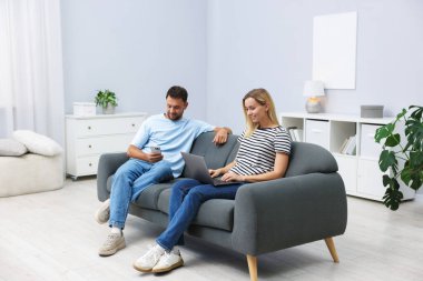 Happy couple with devices spending time together on sofa at home