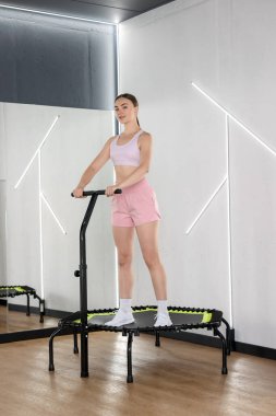 Spor salonundaki aynanın yanındaki trambolinde genç bir kadın.