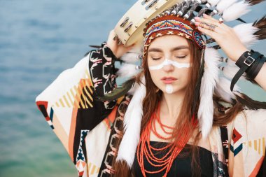 Kızılderili başlıklı güzel şaman kadın. Yüzü boyalı, tef ve mücevherleri nehir kenarında.