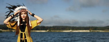 Kızılderili başlıklı güzel bir şaman kadın nehir kenarında yüzünü boyuyor. Metin için boşluk