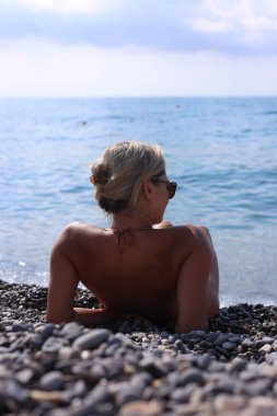 Bikinili bir kadın çakıl taşı plajında yatıyor.