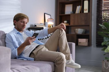 Evdeki koltukta akıllı telefon kullanan bir adam, mesaj için yer.
