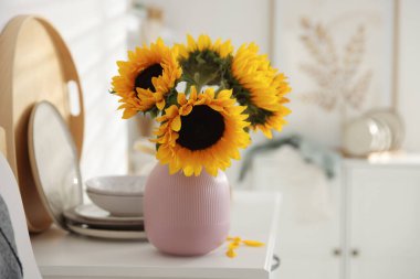 Vazodaki güzel ayçiçekleri ve evdeki beyaz çekmecelerin üstündeki mutfak gereçleri