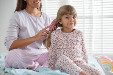 Anne, kızının saçını evde tarıyor, yakın plan.