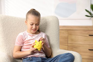 Küçük kız cep harçlığını evdeki kumbaraya yatırıyor.