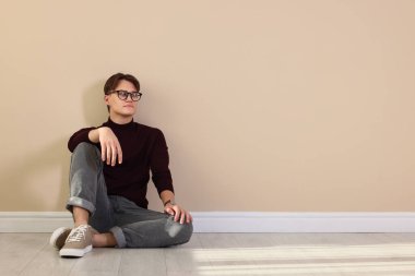 Bej duvarın yanında şık kotlu bir adam.