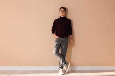 Bej duvarın yanında şık kotlu bir adam var.