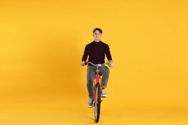 Turuncu arka planda kırmızı bisiklet süren yakışıklı bir adam.