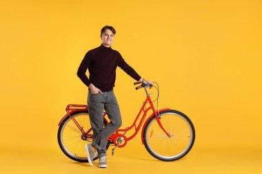 Turuncu arka planda kırmızı bisikletli yakışıklı bir adam.