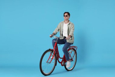 Açık mavi arka planda kırmızı bisiklete binen yakışıklı adam