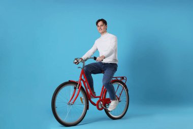 Açık mavi arka planda kırmızı bisiklete binen yakışıklı adam