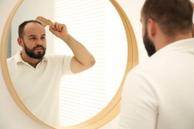Kellik sorunu. Evdeki adam aynanın yanında saçını tarıyor.