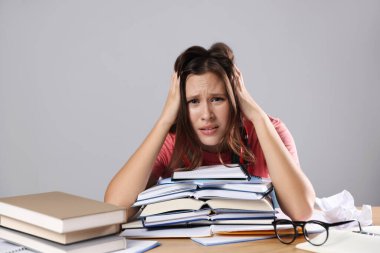 Kitapları olan endişeli öğrenci gri duvarın yanındaki masada sınava hazırlanıyor.