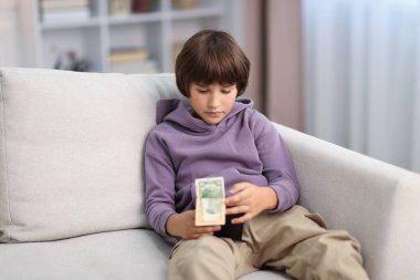 Evdeki kanepede cep harçlığı olan çocuk.