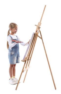 Meslek seçimi. Beyaz arka planda ressammış gibi davranan palet boyalı ve sehpanın yanındaki fırçalı küçük kız.