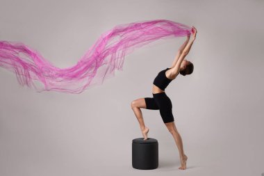 Elbiseli kadın açık gri arka planda jimnastik yapıyor.