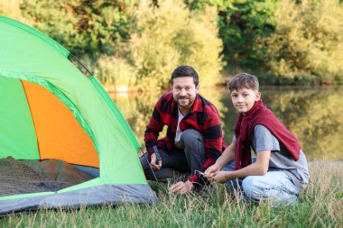 Mutlu baba ve oğul nehir kenarında kamp çadırı kuruyorlar.
