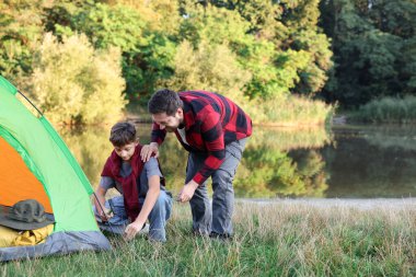 Baba ve oğul nehir kenarında kamp çadırı kuruyorlar. Metin için boşluk