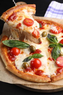 Peynirli, domatesli ve zeytinli lezzetli pizzayı siyah masada yakın plan çekiyoruz.