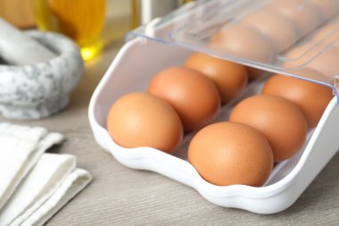 Plastik kabın içinde çiğ tavuk yumurtası ve ahşap tezgahın üzerinde mutfak aletleri, yakın plan.