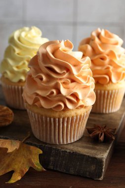 Renkli kremalı lezzetli kekler ve ahşap masada sonbahar dekoru, yakın plan.