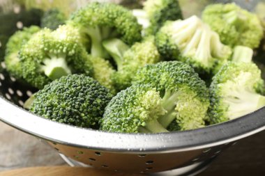 Fresh raw broccoli in colander on table, closeup