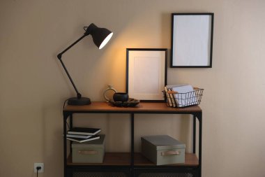 Stylish lamp, other decor and books on console table near beige wall indoors
