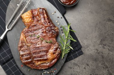 Lezzetli ızgara biftek, otlar, baharatlar, oyma çatal ve ketçap, gri desenli masa, düz yatak. Metin için boşluk