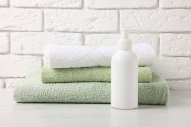 Stack of fresh towel and cosmetic product on white table against brick wall