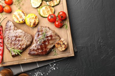 Bitki ve sebzeli ızgara biftekler koyu dokulu masa, düz yatak. Metin için boşluk