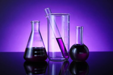 Masada mor arkaplana karşı renk sıvısı bulunan farklı bir laboratuar cam.